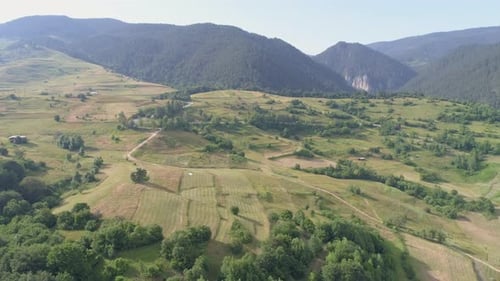 AERIAL: flying over arable land in a mountainous area, mountains can be seen in the background.