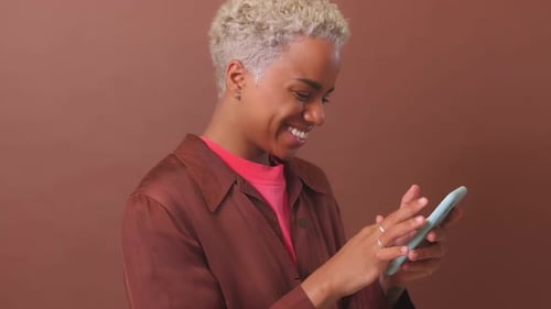 Woman Smiles Using Mobile Phone Against Brown Background