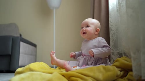 Una linda niña con un vestido morado está sentada en el suelo, riendo y jugando