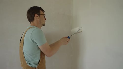 Man Painting Wall With Paint Roller Indoors