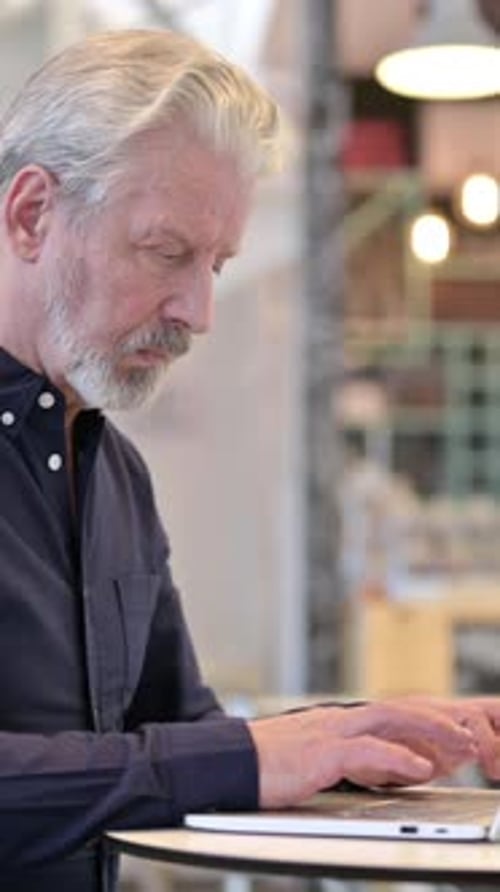Old Man Using Laptop in Cafe, vertical video