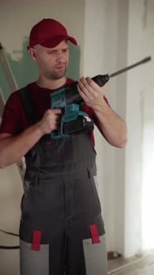 Construction Worker Inspecting Rotary Hammer Drill During Renovation Work