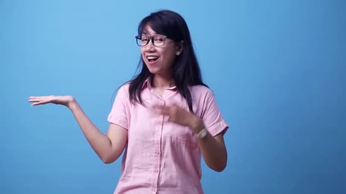 Happy young Asian woman showing something on her hands. Isolated on blue background in studio