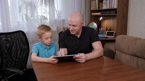 Young Boy Using Tablet with Adult at Table