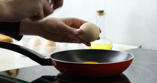 Woman cracking egg into frying pan in kitchen, closeup