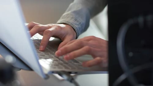 Hands settling on laptop keyboard at desk are typing code steadily for completing project at work