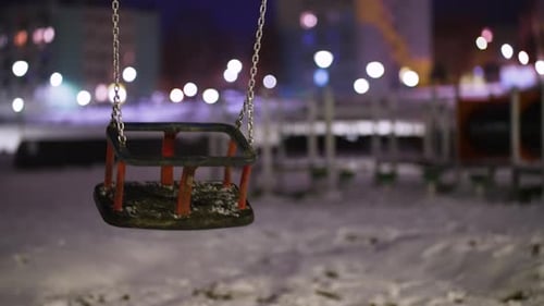 Empty Children Playground at Park with Kid Swing Swinging in Cold Winter Night with Snow on Ground