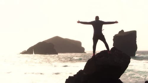 Silhouette of man standing at the beach over a rock with open arms. Vcations at the seashore concept