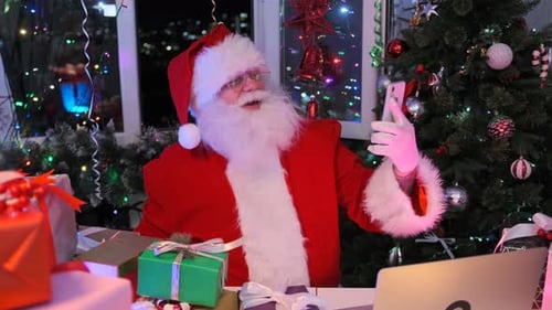 Friendly Santa Claus with smartphone in hand waves, talking and laughs via video call