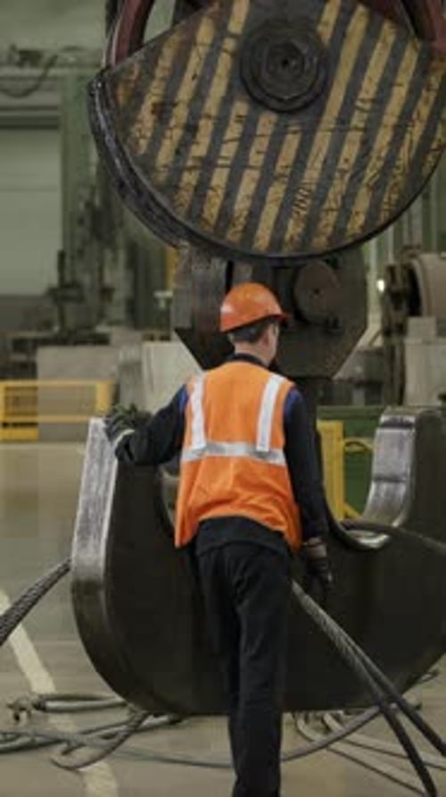 Workers Securing Equipment with Overhead Crane in Factory