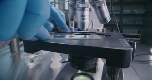 Close Up of Microbiologist Putting Glass Slide with Test Sample Under Microscope