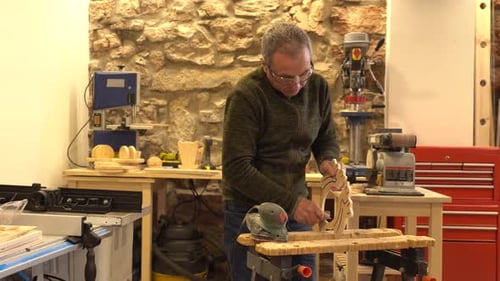 Carpenter using an electric tool to polish a piece of wood in studio workshop