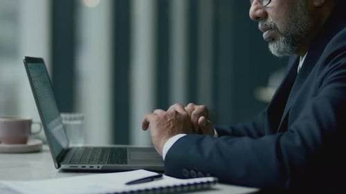 Businessman Reviewing Charts on Laptop Screen at Table in Cafe