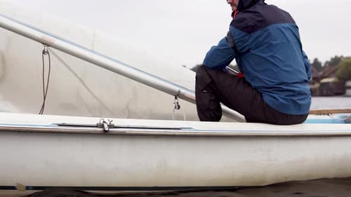 A yachtsman walks along the river on a sailboat with a lowered sail in the cold season.