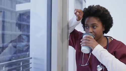Tired african american female doctor drinking coffee in hospital, slow motion