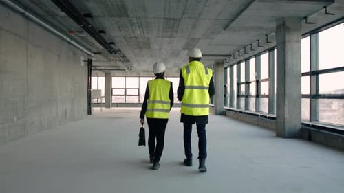 Rear View of Man and Woman Engineers Walking on Construction Site, Talking