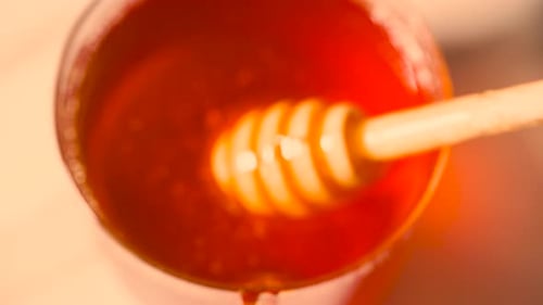 Pingando mel do gotejador de madeira na jarra de vidro Derramando mel. Comida orgânica saudável. Fechamento macro