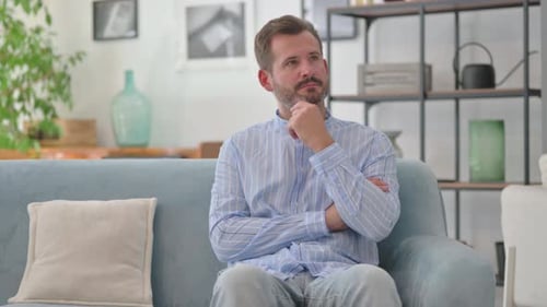 Nachdenklicher Mann mittleren Alters sitzt zu Hause auf dem Sofa