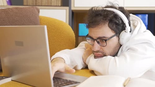 Tired Man Working on Laptop Wearing Headphones Indoors