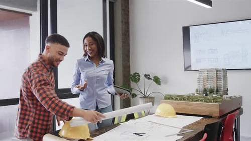 Happy diverse male and female architects with tablet discussing blueprints in office, slow motion