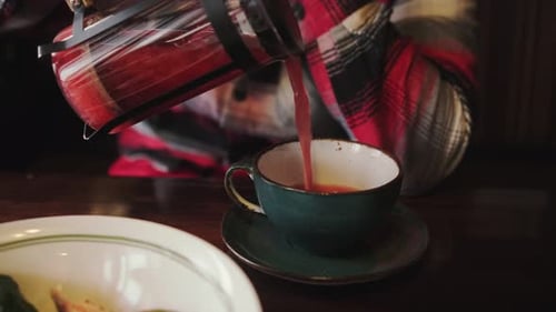 Mann gießt heißen Tee aus einer Teekanne drinnen in eine Tasse
