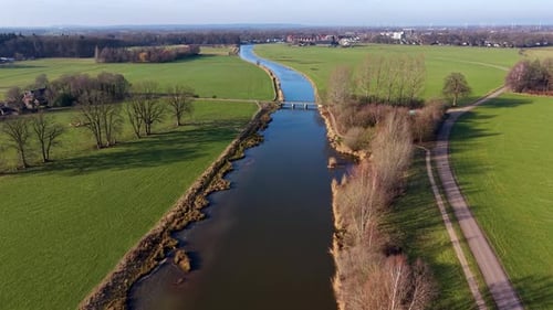 Aerial view of a rural landscape with a canal curving through green fields, two small road bridges