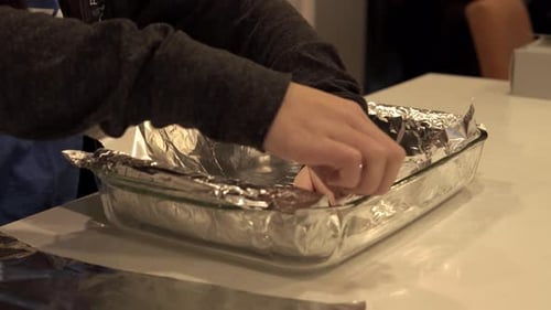 A girl lays out aluminum foil on a baking tray as prep for baking some cookies