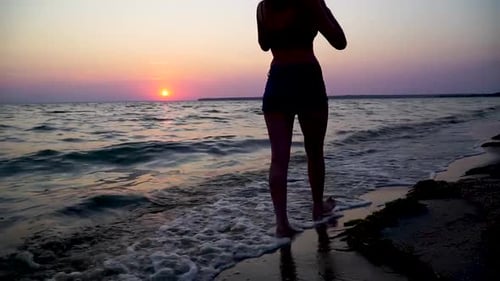 Girl walking on the sunset beach in front of waves on the sea