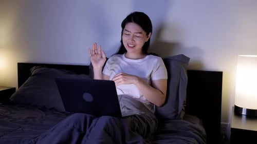 Asiatische Frau bei einem Videoanruf im Bett.