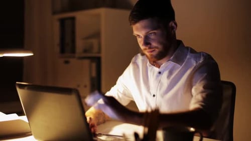 Man Working on Laptop and Writing at Night