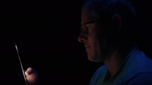 Man's Face Lit By Phone Screen In Dim Room