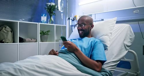Mobile, smile and man in bed in clinic for typing message, laugh and medical update for recovery