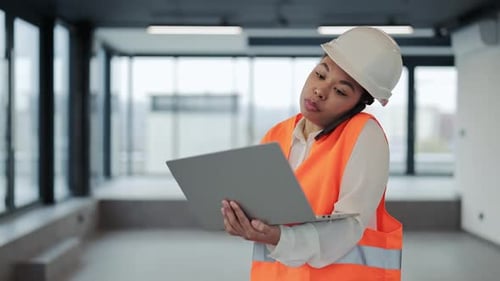 Female Engineer in Hardhat Inspects Construction Site Discussing Plans on Phone and Using Laptop
