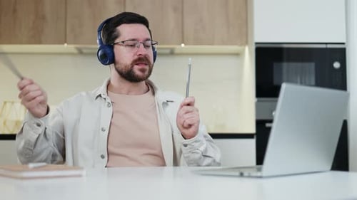 Homme caucasien utilisant des stylos comme pilons tout en étant assis devant un bureau avec un ordinateur