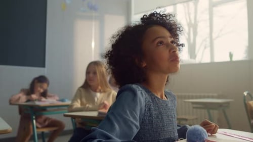 Positive african american schoolgirl talks with teacher during lesson in classroom