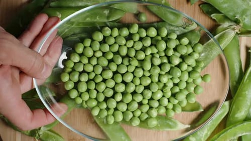 Top view, bringing the cleaned green peas closer to the camera and shaking the plate, slow-motion.