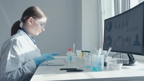 A Female Researcher Sits at a Workplace in a Laboratory Behind a Personal Computer Monitor
