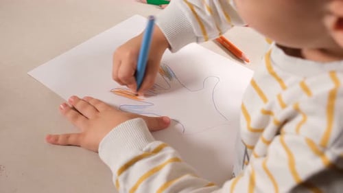 Child Drawing Hand with Colored Crayons on Paper