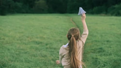 Little Girl Runs With Paper Airplane on Grass Field