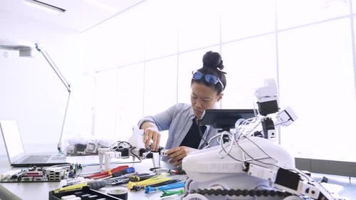 Ingeniera asiática ensamblando robótica con habilidad en un laboratorio brillante