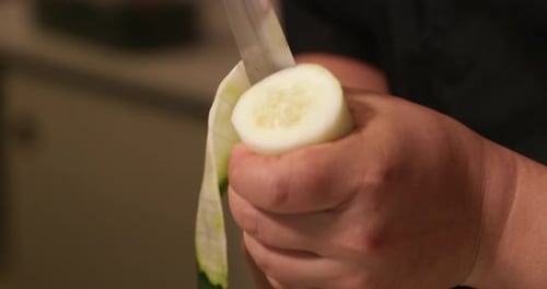 Un chef tient le concombre dans une main et le coupe en tranches sur toute la circonférence pour en faire une feuille de concombre