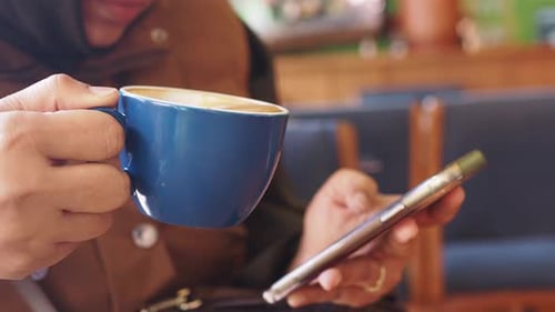 Enjoying Coffee While Browsing on a Smartphone in a Cozy Cafe
