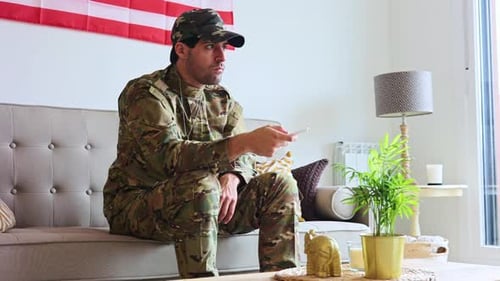 Man in Camouflage Sits on Couch with Remote