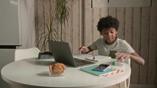 Boy Studying at Home with Laptop and Notebook