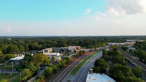 Forwards fly above road and railway line in town outskirts. Several buildings and extensive wooded f