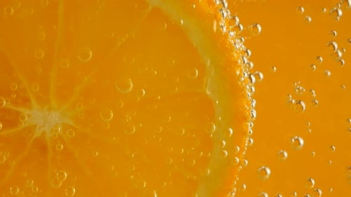 Eine Scheibe reifer Orange im Wasser sprudelt auf einem orangefarbenen Hintergrund.