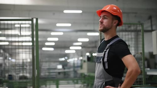 Worker in uniform looks around in factory and taking off orange hard hat