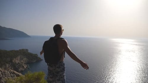 Unrecognizable Hiker with Backpack Standing on Edge of Mountain and Victoriously Raising Hands Male