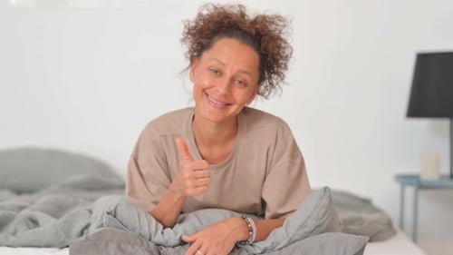 Pouce levé par une femme hispanique alors qu'elle était allongée sur le ventre dans son lit