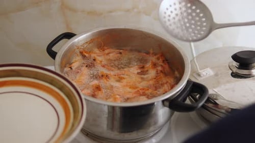 Person Takes Boiled Red Shrimps Out of Boiling Pot with Slotted Spoon